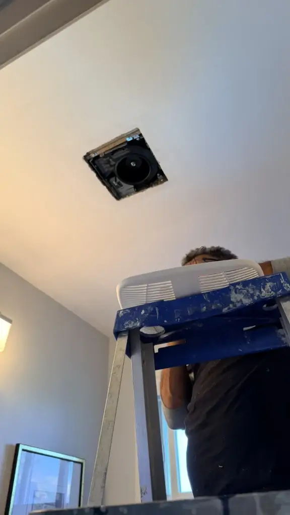 Technician securing the exhaust fan housing from a ladder